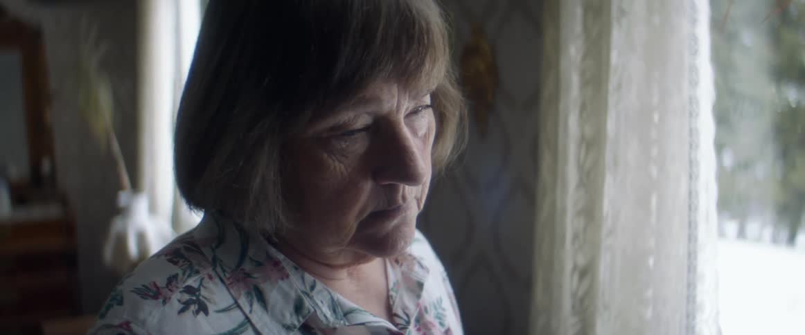 A woman with a grief stricken look on her face staring out of a window from indoors in a bedroom at daytime