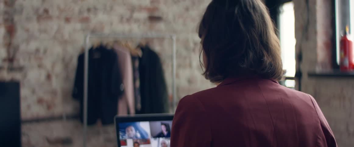 A woman sitting at a desk in a living room at home talking to friends in a video call on a laptop during the day