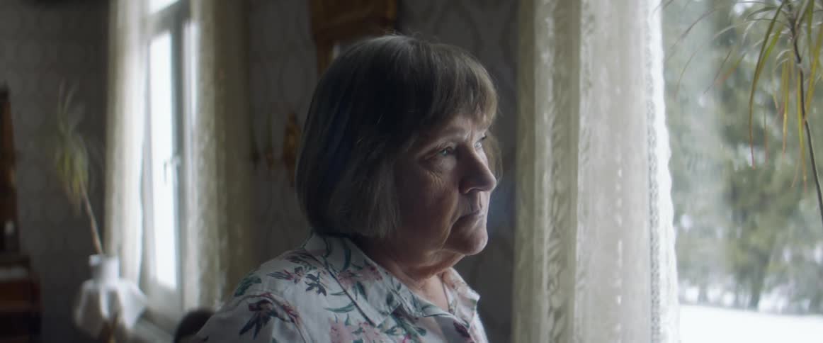An elderly woman looks out the window of her home