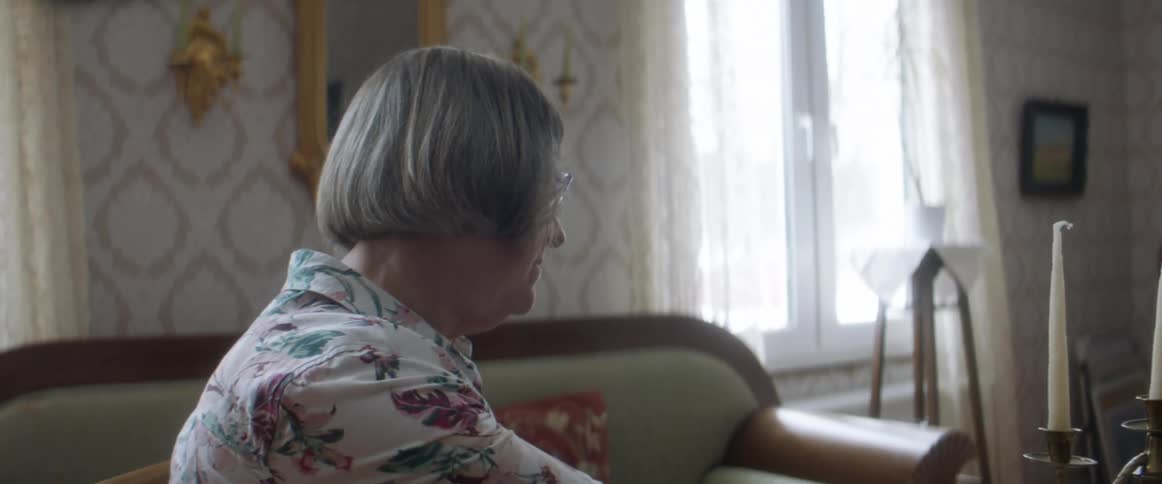 An old woman sitting in a room at home during the day