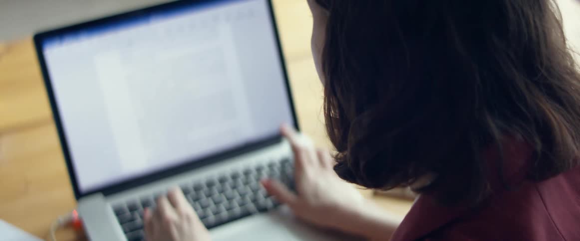 A woman makes a note then goes back to typing a paper on a laptop