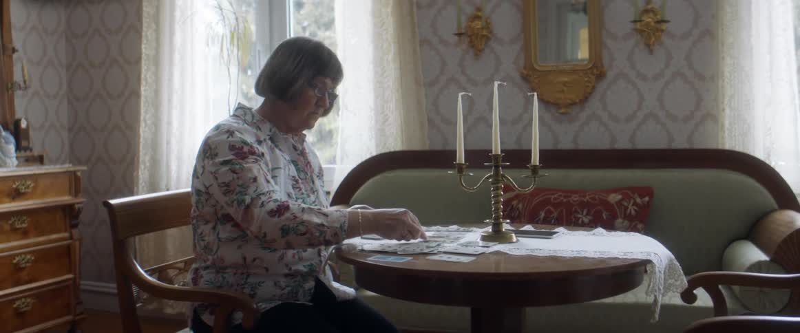 A woman sitting at a small circle table playing with poker cards laid out on the table indoors at daytime