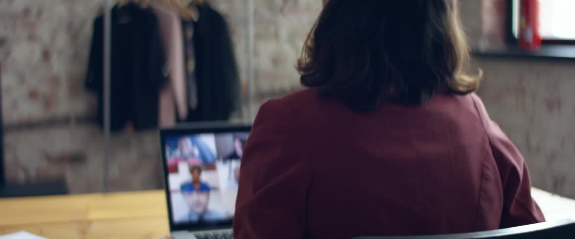 A woman sitting at a wooden desk indoors talking to her friends on a laptop computer in a video call