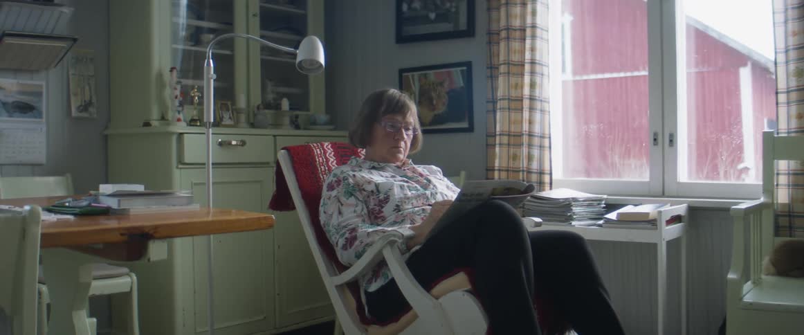 A woman sits in a rocking chair at home and reads a magazine