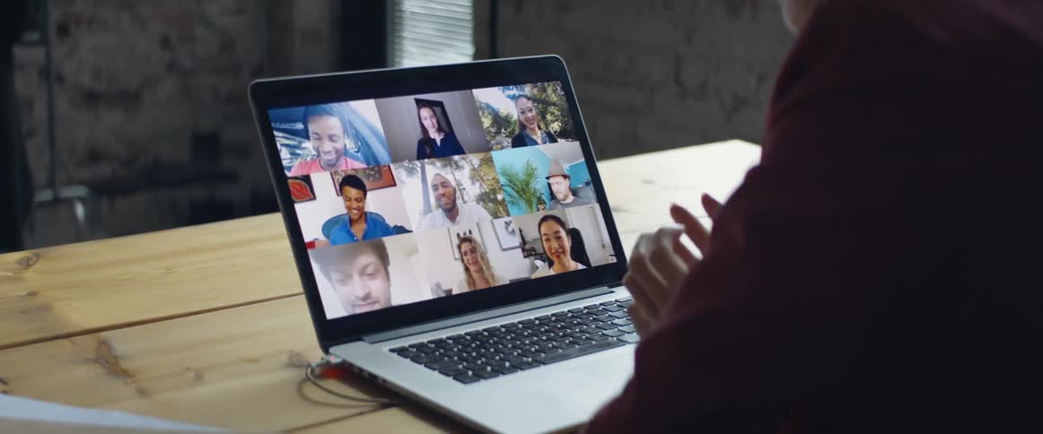 A person sitting at a table on a zoom call with several people on a laptop