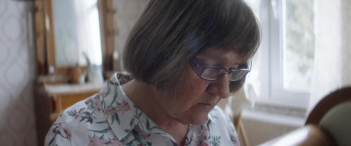 A woman in a room with glasses with a wall and a window in the background