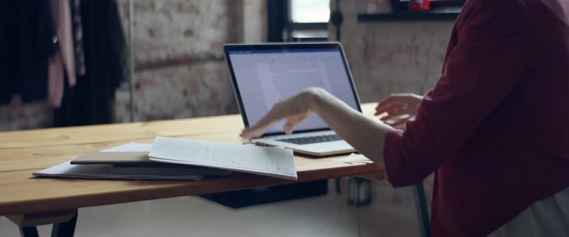 A woman sits at a desk and works on a laptop