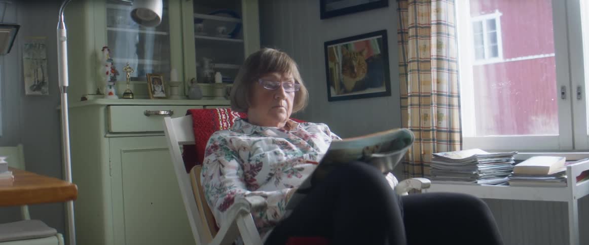 A woman in a room sitting on a rocking chair with a wall and window in the background