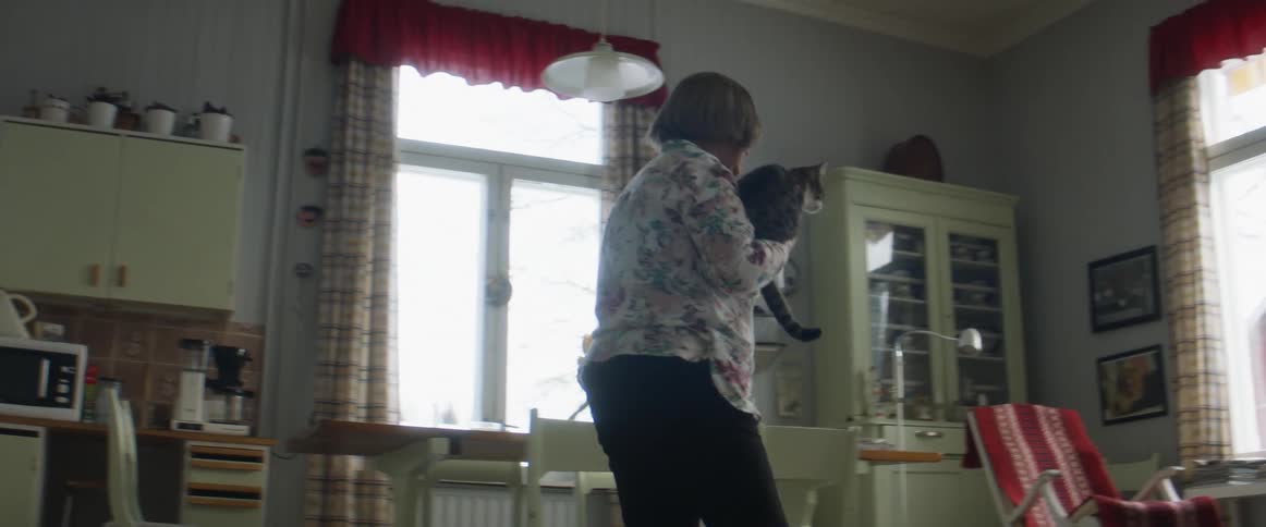 A woman picking up a cat and going to sit down with it