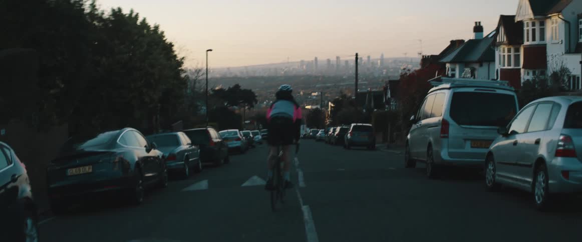 A person with a helmet riding a bike on a neighborhood street with the sky and clouds in the background