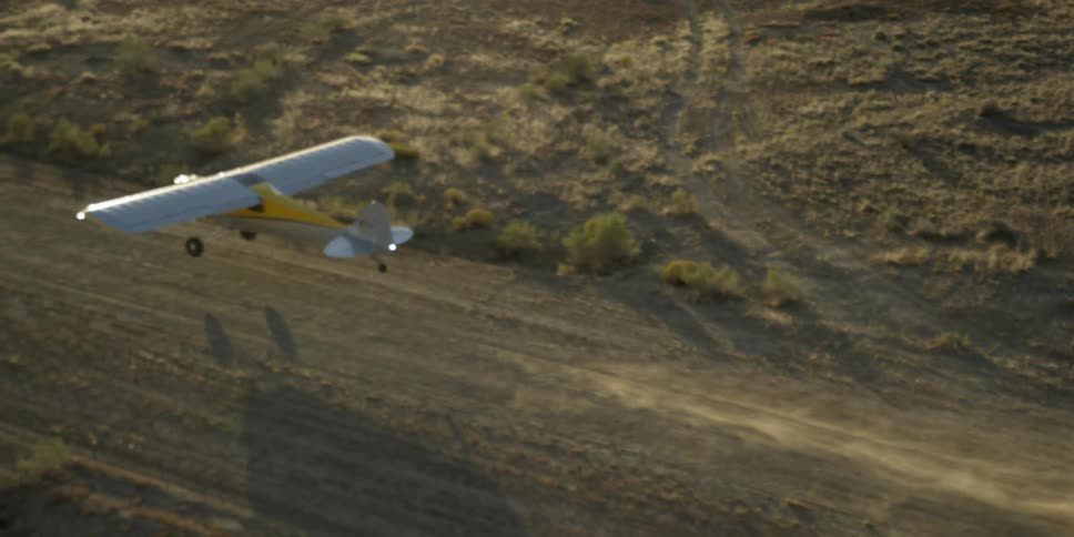 A plane slowly takes off from a dirt runway