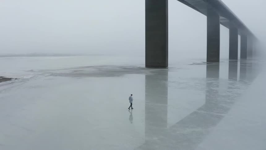 A man walking on ice across a river near a bridge