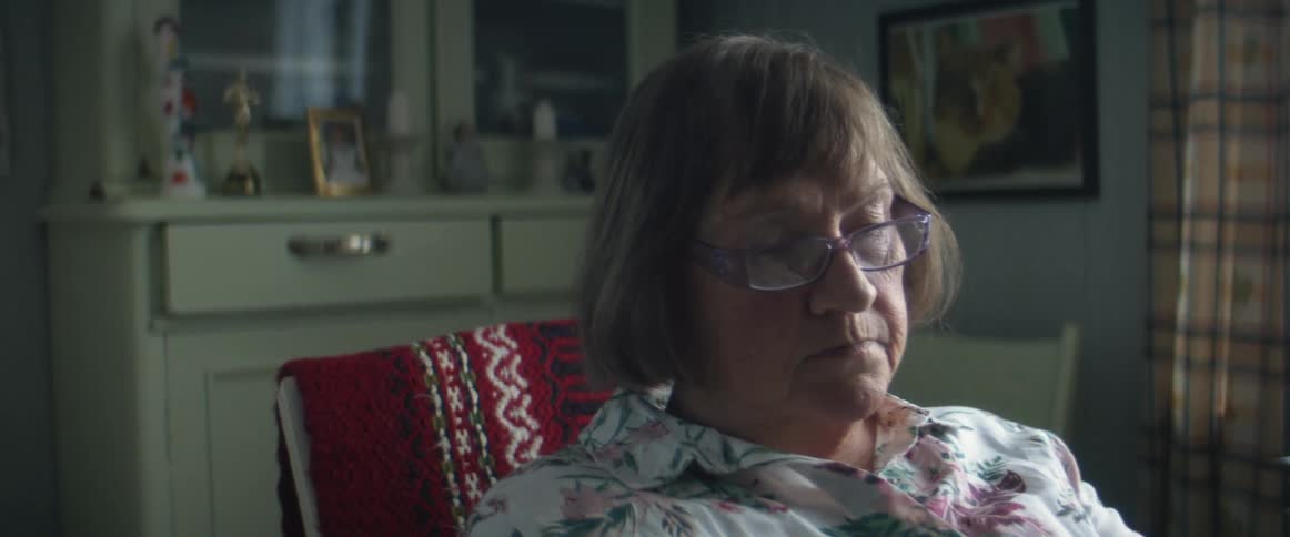 A woman in a room with glasses with a wall and a window in the background