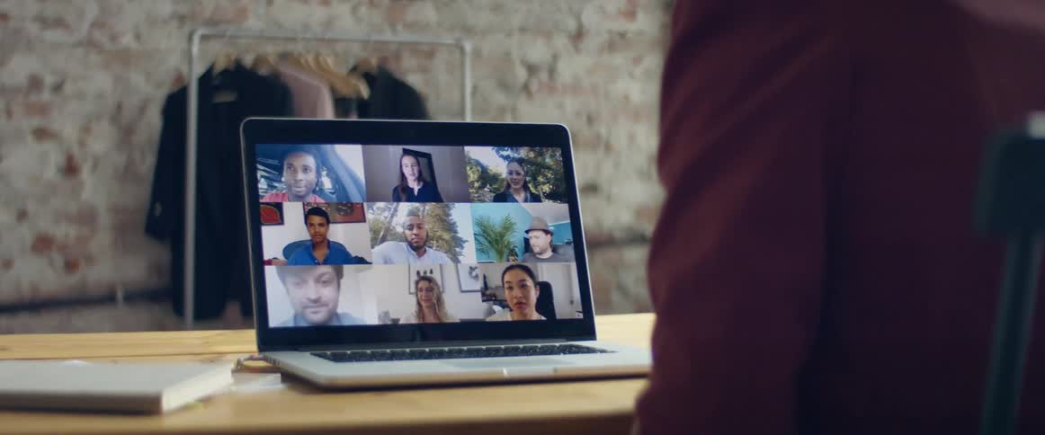 A woman gestures with her hand while sitting at a desk meeting with several people via video conference on her laptop