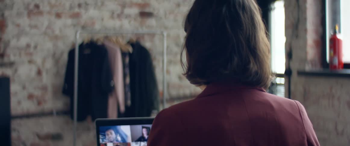 Woman sitting at a desk in her office talking to a group of friends through a video call on a laptop