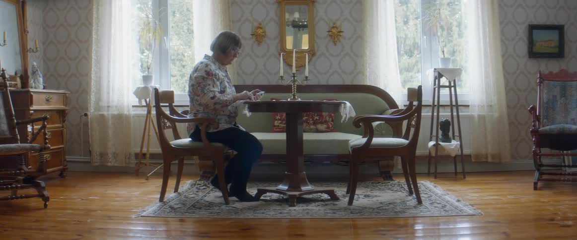 An elderly white woman sitting and handling cards at a table in the living room