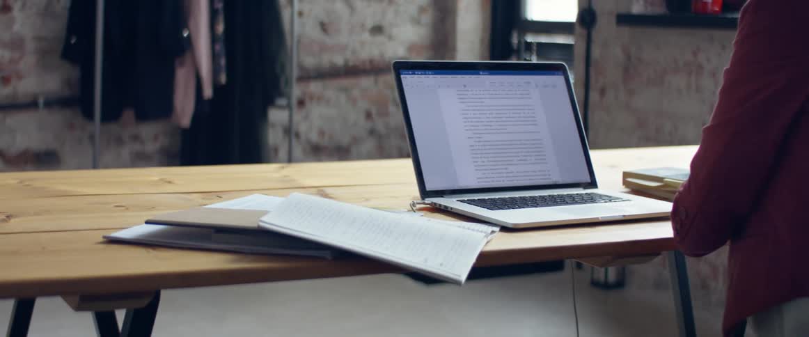 A woman makes a note on a post it and sticks it to a page in a notebook before typing on her laptop