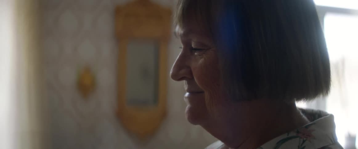 A woman in a room smiling with a wall and window in the background