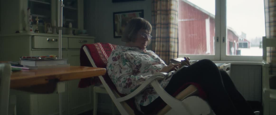 An elderly woman sits inside and types on a cell phone