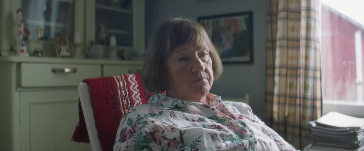 An elderly woman sits in a chair looking sad and depressed