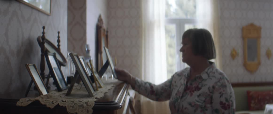 A woman in a room picking up a picture frame with a wall and window in the background