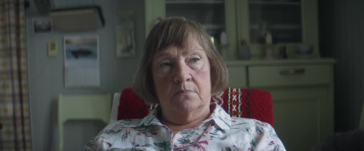 An elderly woman sits in a chair looking sad and depressed