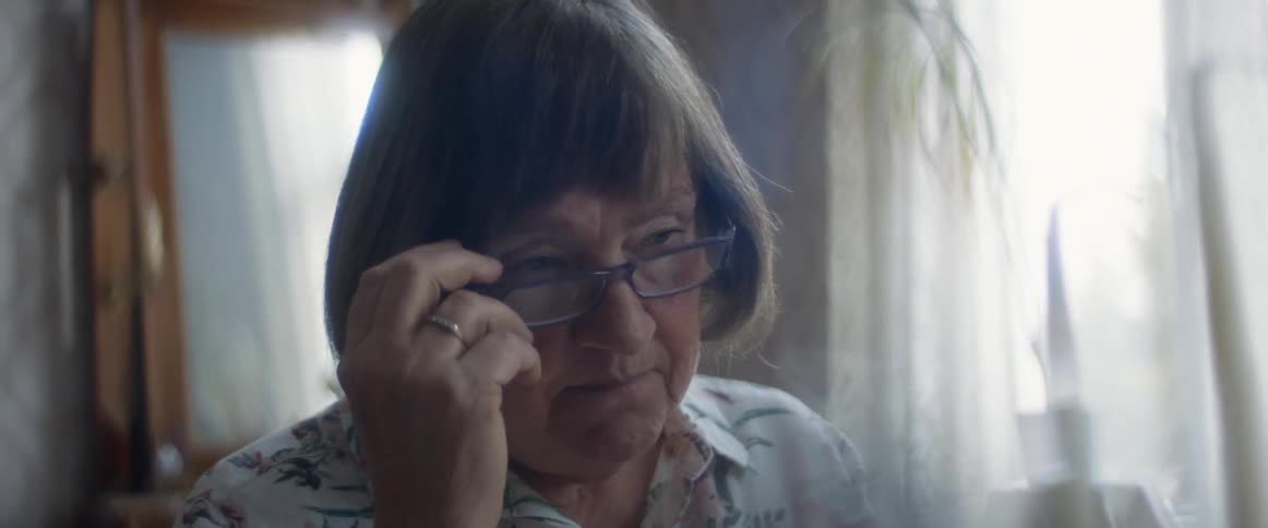 A woman in a room taking off her glasses with a wall and window in the background