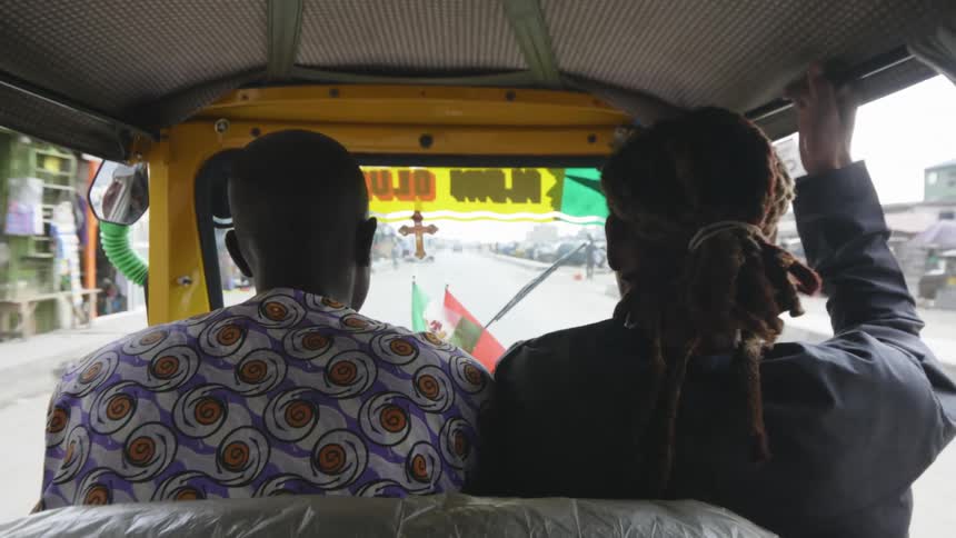 Two people riding a rickshaw driving on the street of a small city