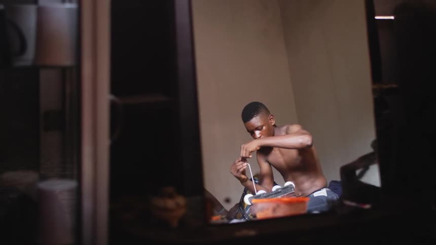 A young man kneeling on the floor in a room fiddling with a device in his lap