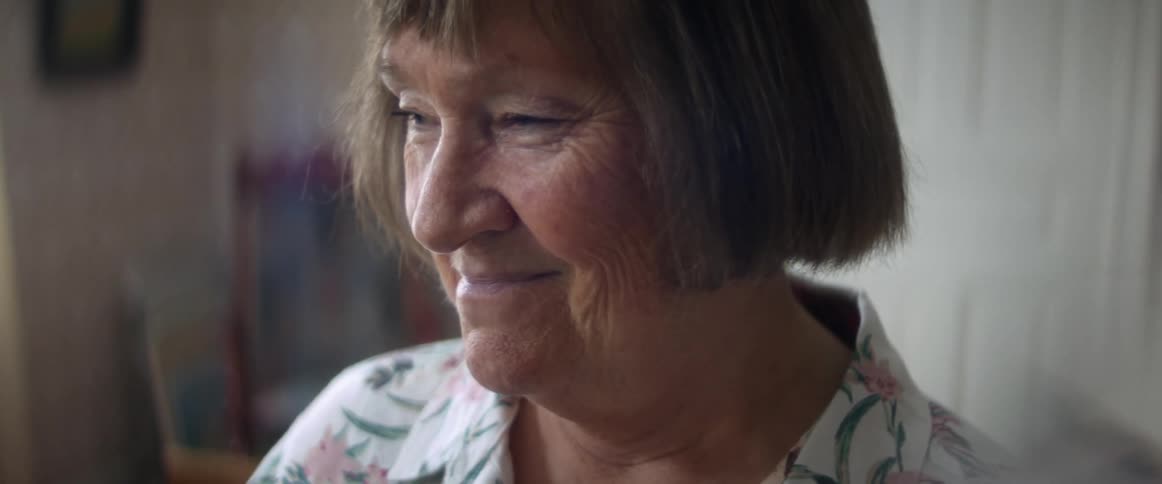 A woman in a room smiling with a wall and window in the background