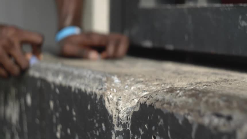 A person with a wristband rubbing a stone on concrete next to a door