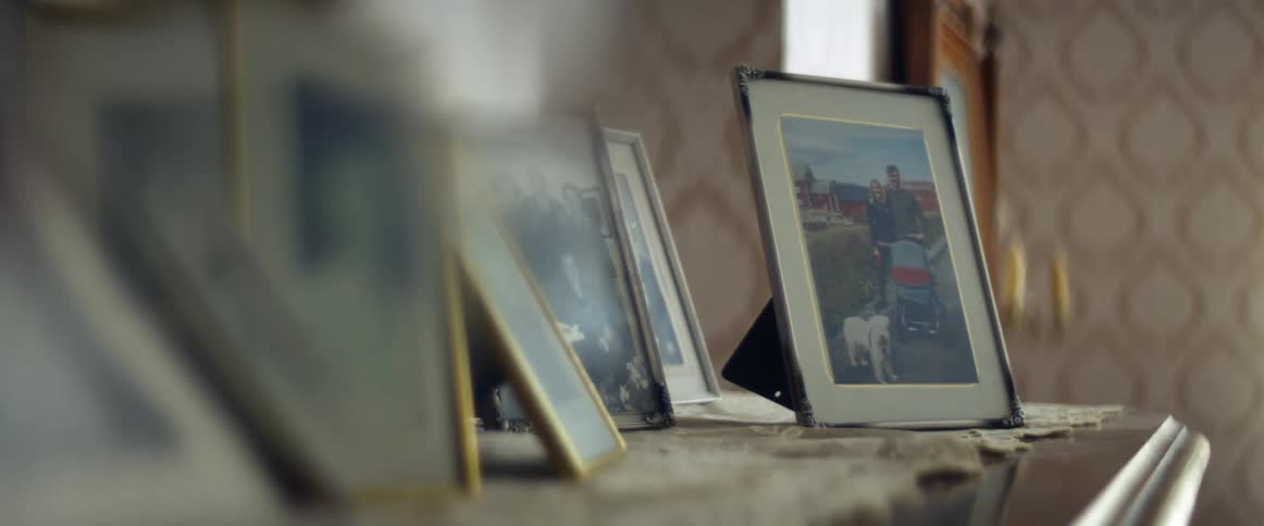A room with picture frames with a candlestick a wall and window in the background