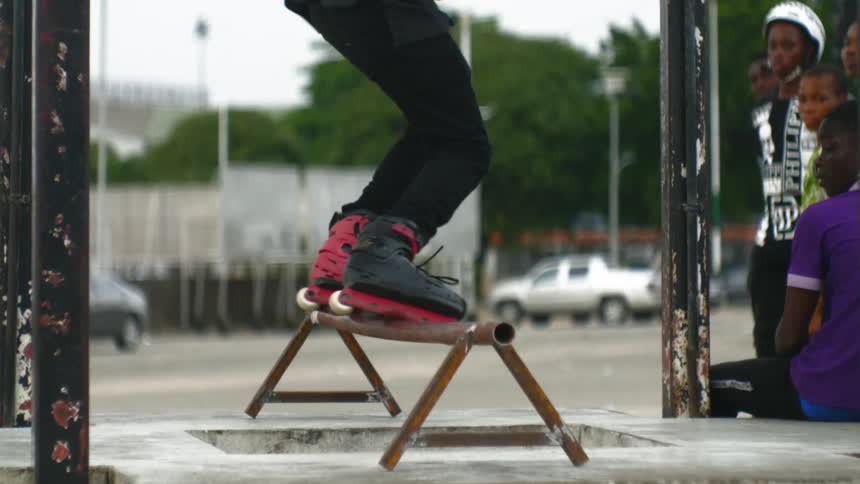 A man roller skates and jumps and crosses a bar as a group of kids watch him