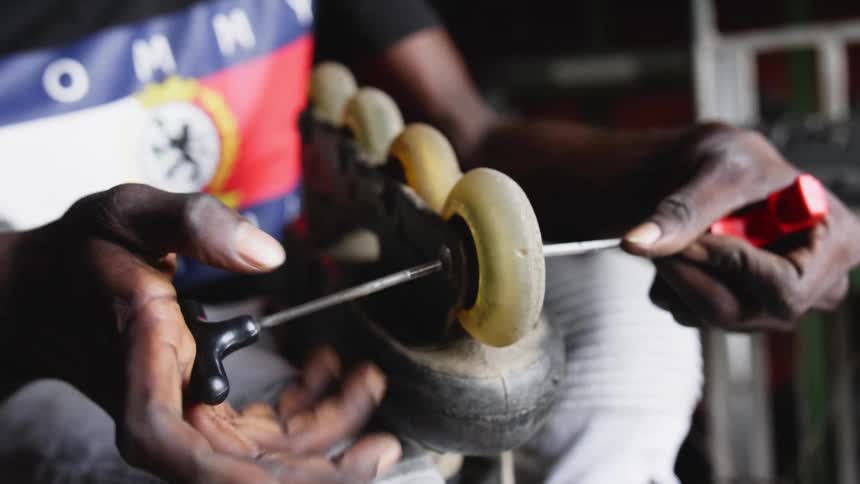 A man holds a rollerblade in his lap and uses two skate tools to tighten the wheels
