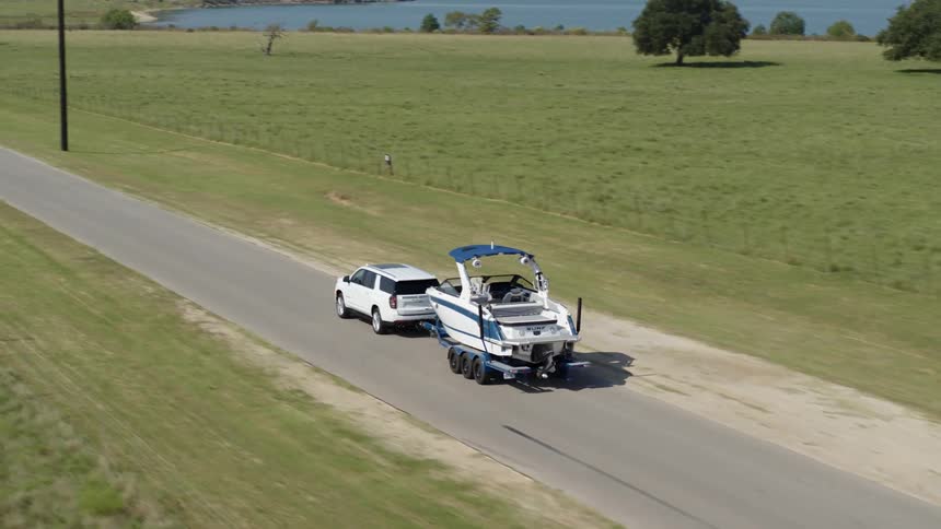 A white truck pulls a motor boat down the road with a lake in the distance
