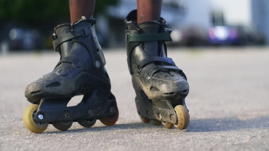 A person with in line skates with vehicles trees and a building in the background