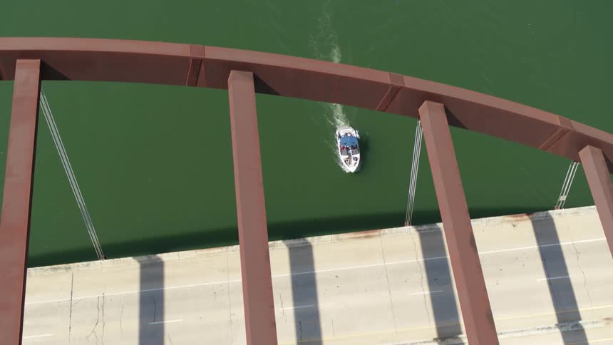 A small speedboat travels under a bridge over a river