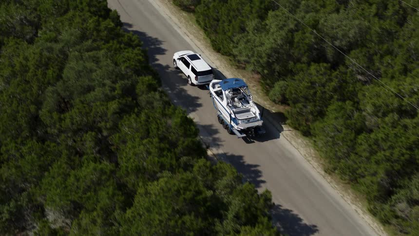 An aerial view of a suv towing a boat down the road