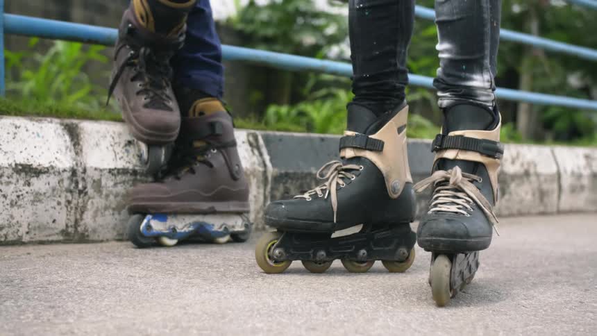 Two people with only their legs showing wearing rollerblades outside
