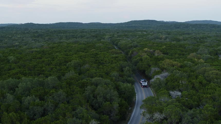 White truck pulling a boat travels on a road through a forested area
