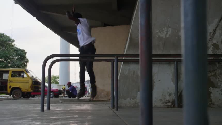 A man with in line skates jumping and skating on a pole with trees the sky and clouds in the background