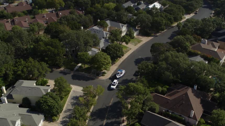 A vehicle towing a boat on a neighborhood street with houses and trees