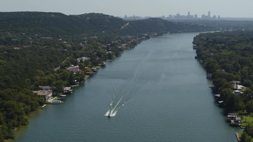 A river with a boat surrounded by trees with the city skyline the sky and clouds in the background