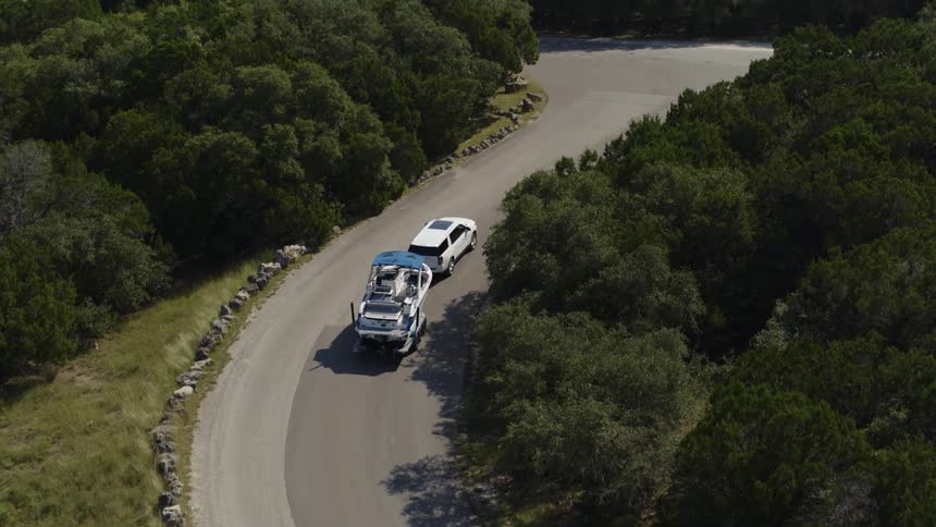 An suv trails a boat on narrow curving road heading towards a mountain lake
