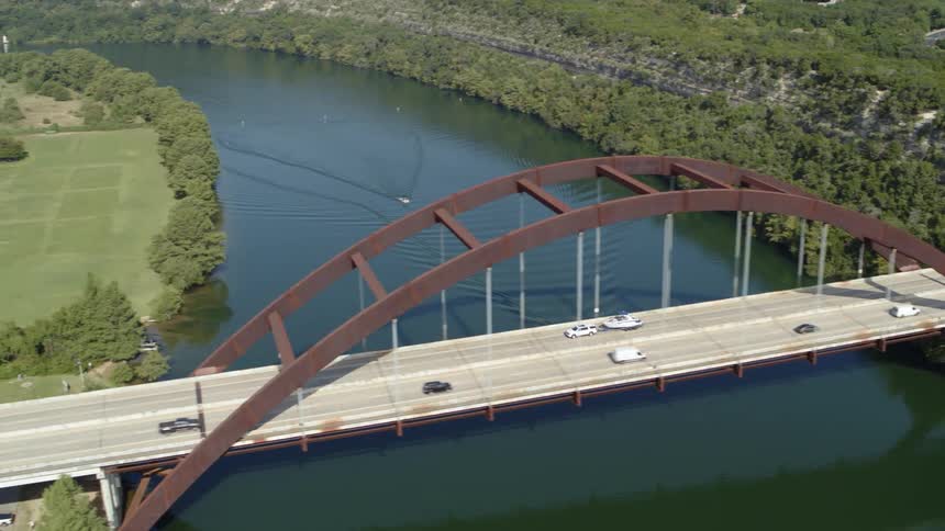 Car towing a boat crossing an arched bridge over a river