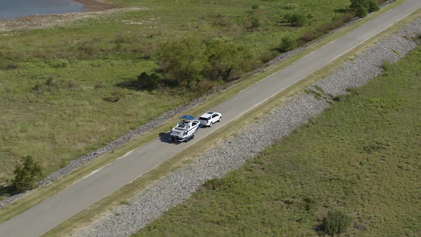 Suv tows boat along road bordered by gravel through fields