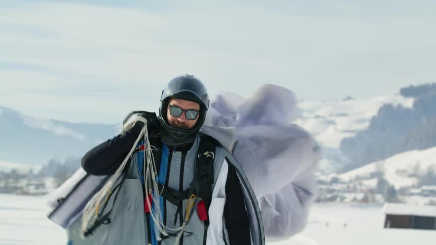 Man collects para sail cloth then walks away near snow covered town nestled against mountains