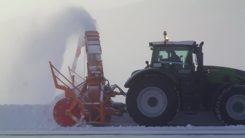 A man drives a snowplow down a snow covered road