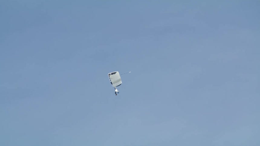A parachutist gliding on a white parachute on the blue sky at daytime
