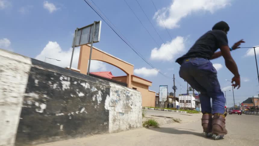 A young male skates along the side of the street where he jumps to perform a trick maneuver atop a wall